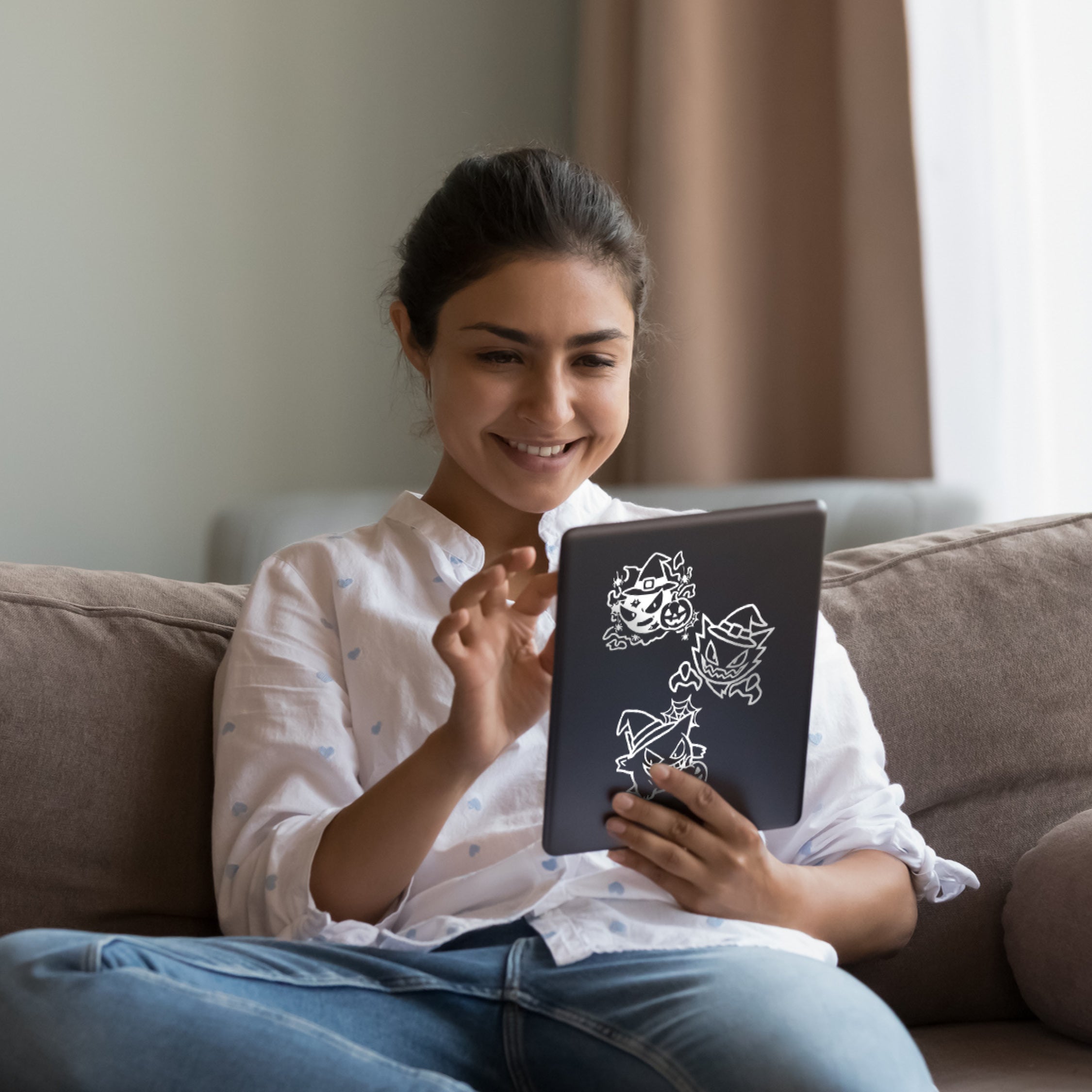 Woman sitting on a couch holding a tablet with a design on the screen.